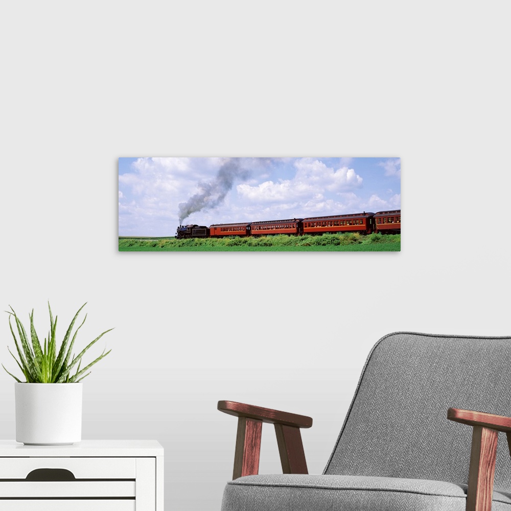 A modern room featuring Panoramic photograph on a large canvas of a steam train with red cars moving down a track surroun...