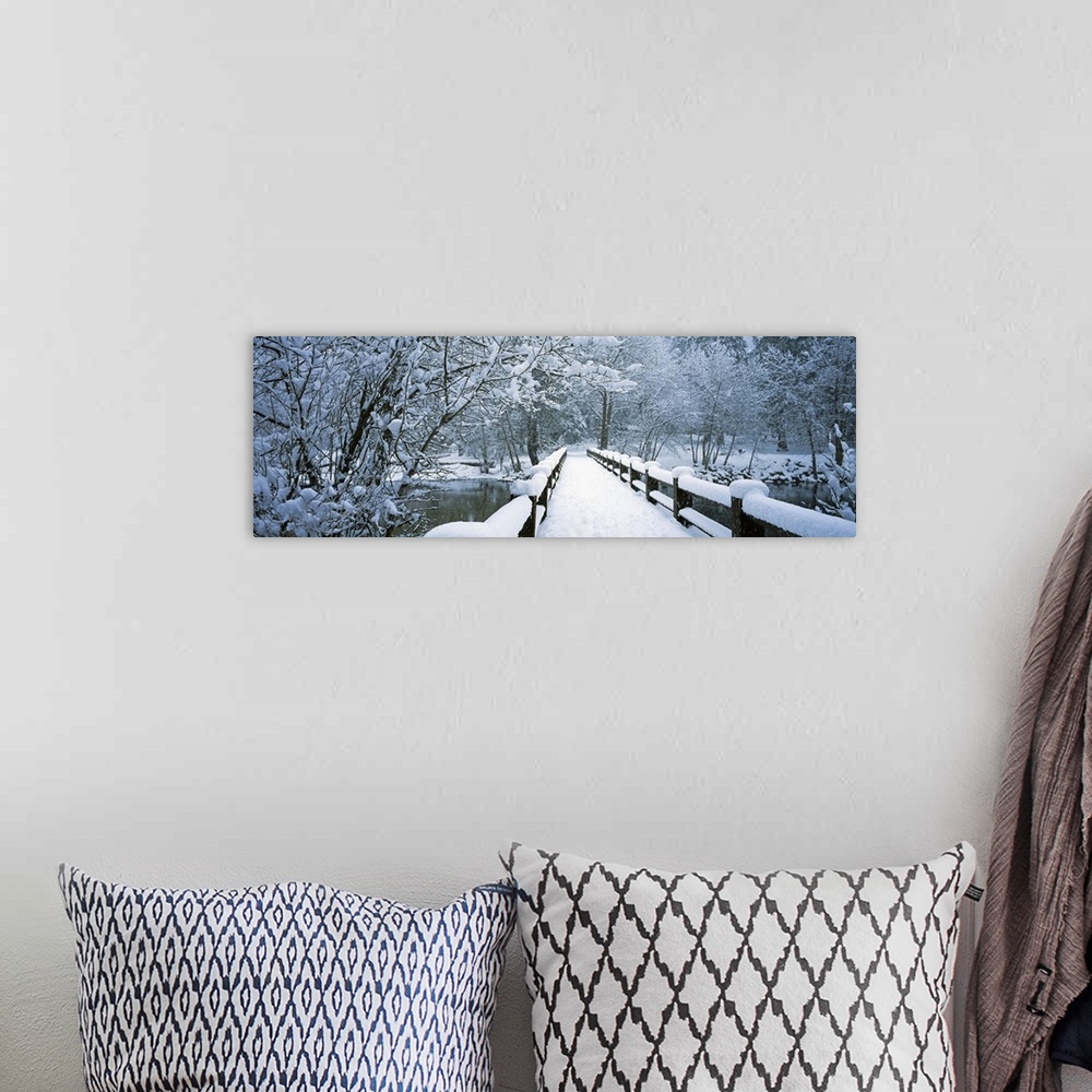 A bohemian room featuring Large panoramic piece of a small bridge that is covered with inches of snow and surrounded by sno...