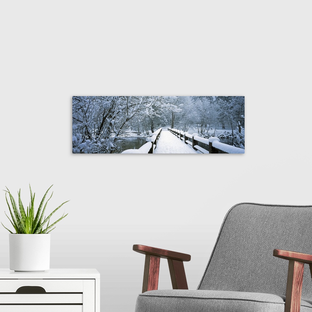 A modern room featuring Large panoramic piece of a small bridge that is covered with inches of snow and surrounded by sno...
