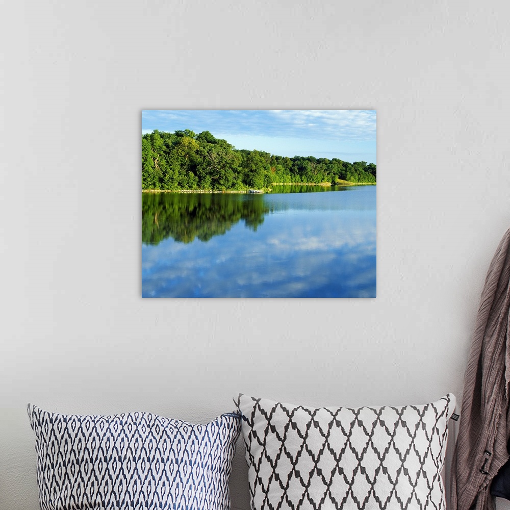 A bohemian room featuring Thick forest curves and lines a large body of water while reflecting in it.
