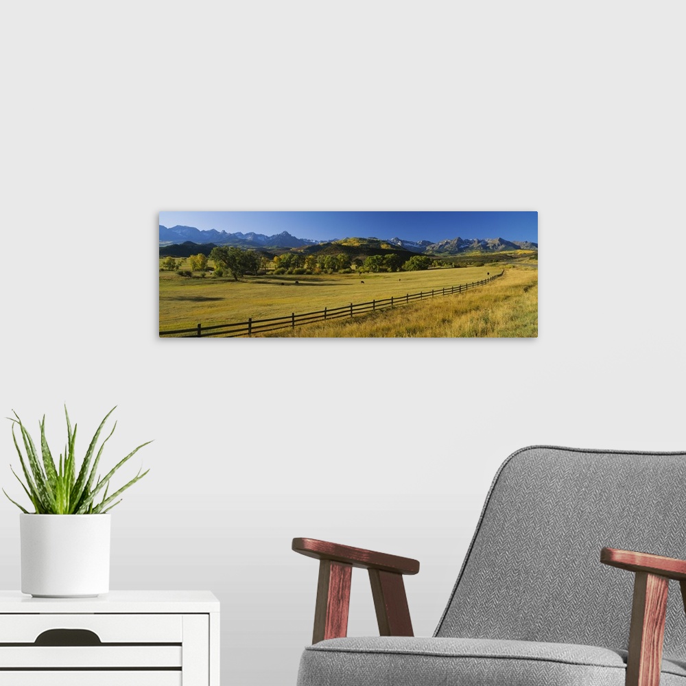 A modern room featuring Wide angle photograph on a giant canvas of a wooden fence running alongside an vast field with tr...