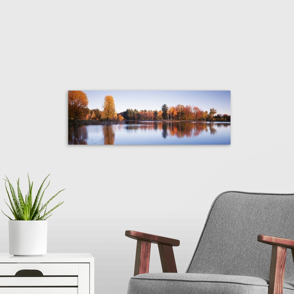 A modern room featuring This photograph is taken behind a body of water of fall colored trees that line the other side of...