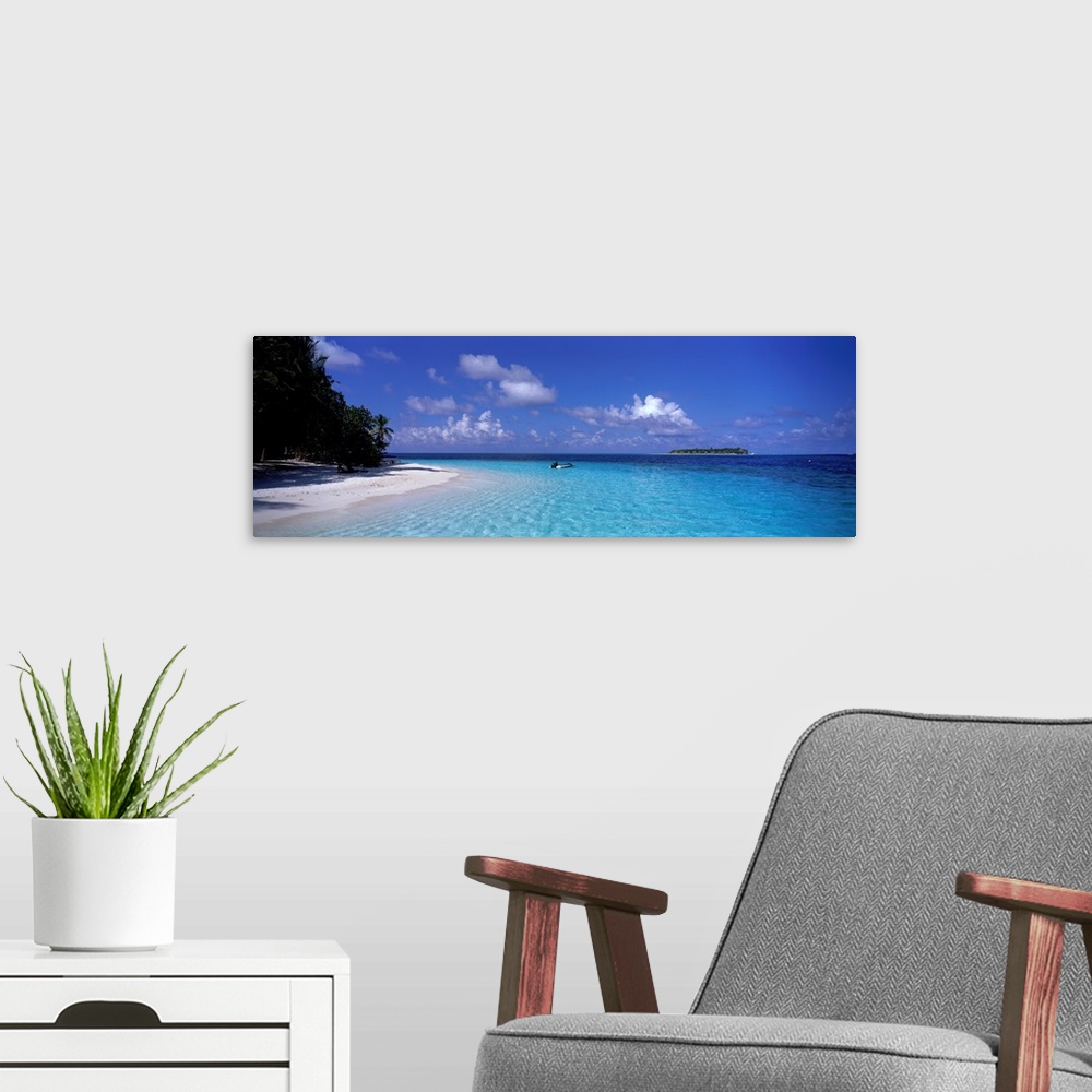 A modern room featuring This wide angle photograph is taken of clear ocean water that has a single boat sitting in it wit...