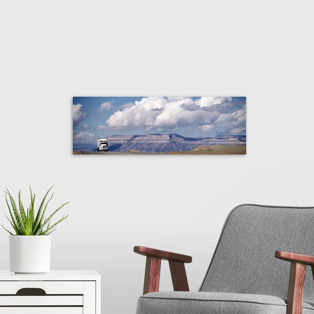 A modern room featuring Panoramic photograph of semi-truck, big rig on highway with canyon in the distance under a cloudy...