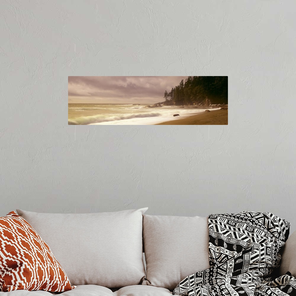 A bohemian room featuring Panoramic picture of waves hitting the shore as the sun peaks through the cloudy sky.