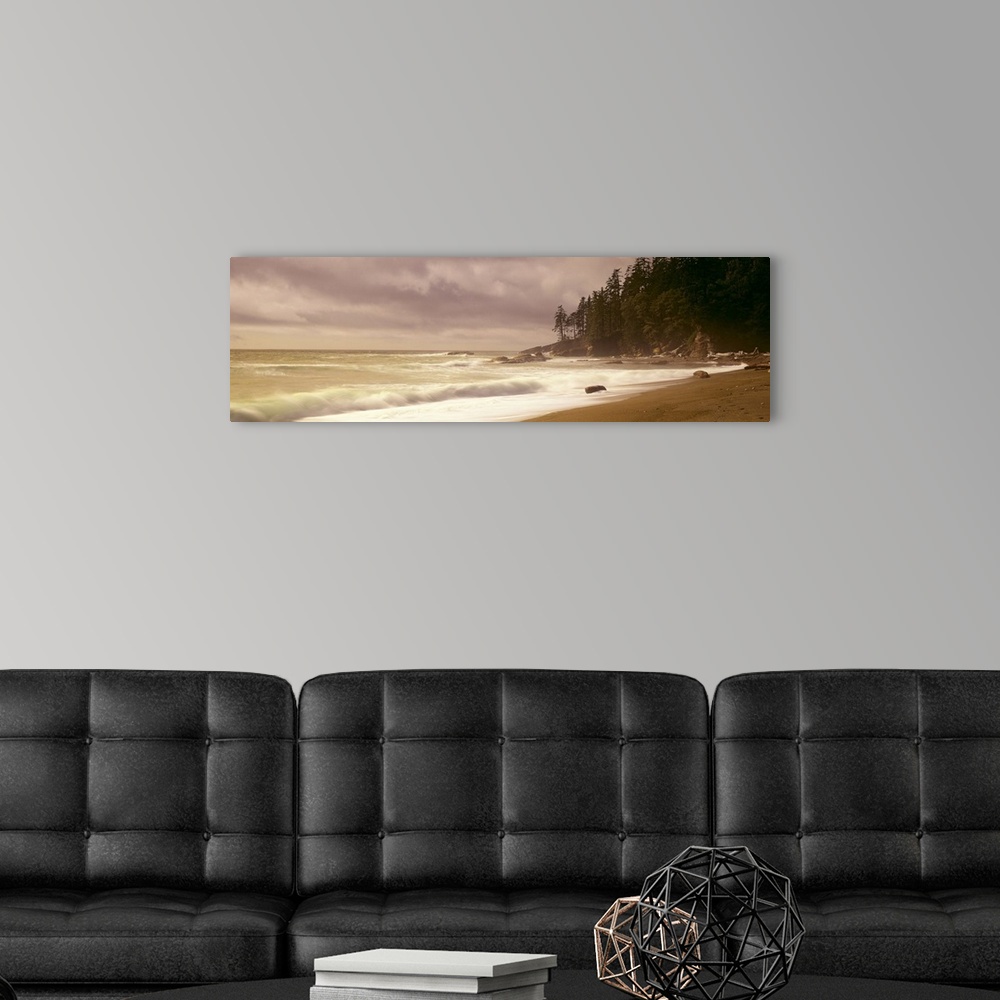 A modern room featuring Panoramic picture of waves hitting the shore as the sun peaks through the cloudy sky.