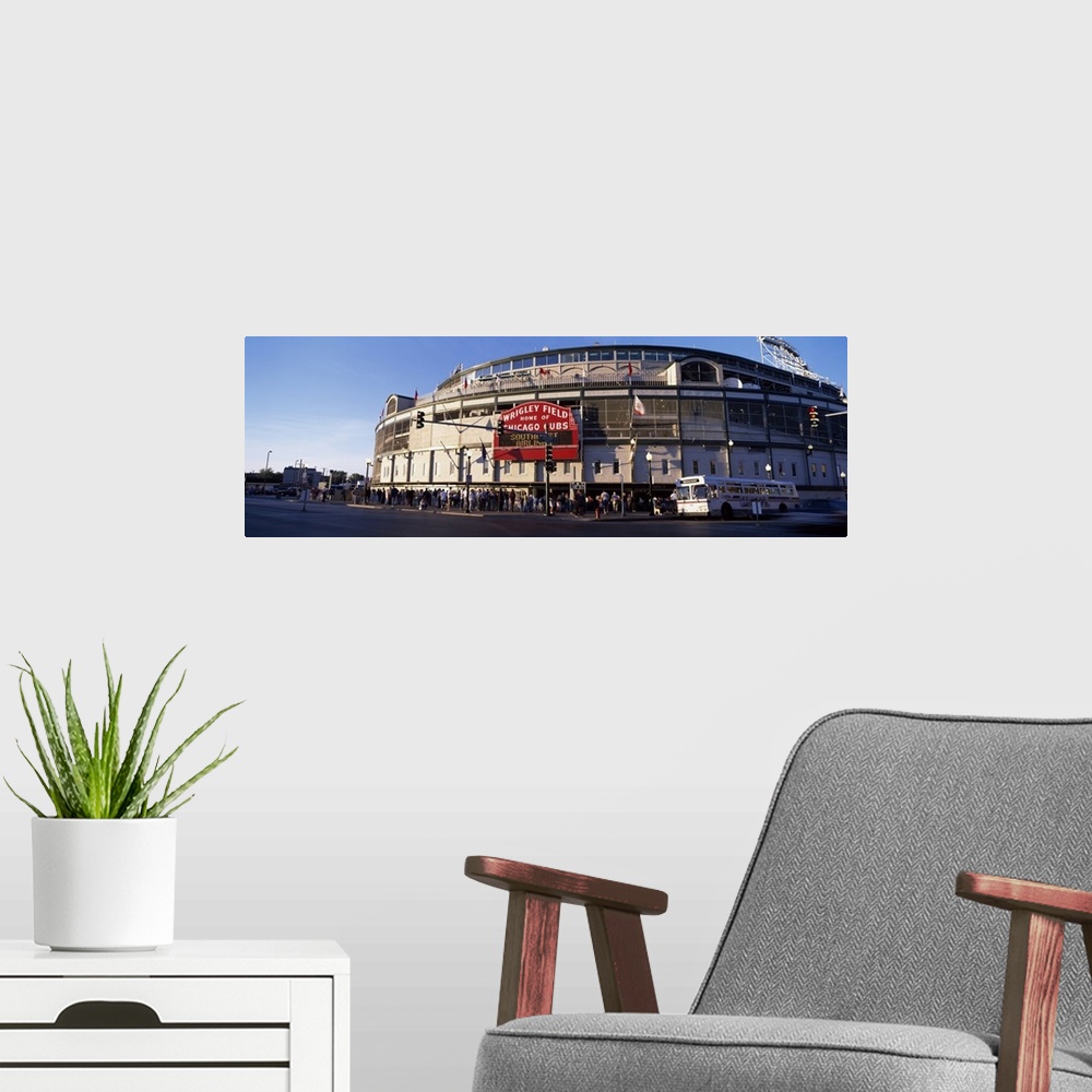 A modern room featuring Wrigley Field is photographed in wide angle view with crowds standing in the front of the stadium...