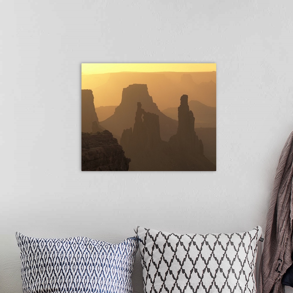 A bohemian room featuring The large rock formations in Canyonlands National Park is silhouetted by the sunset that is out o...