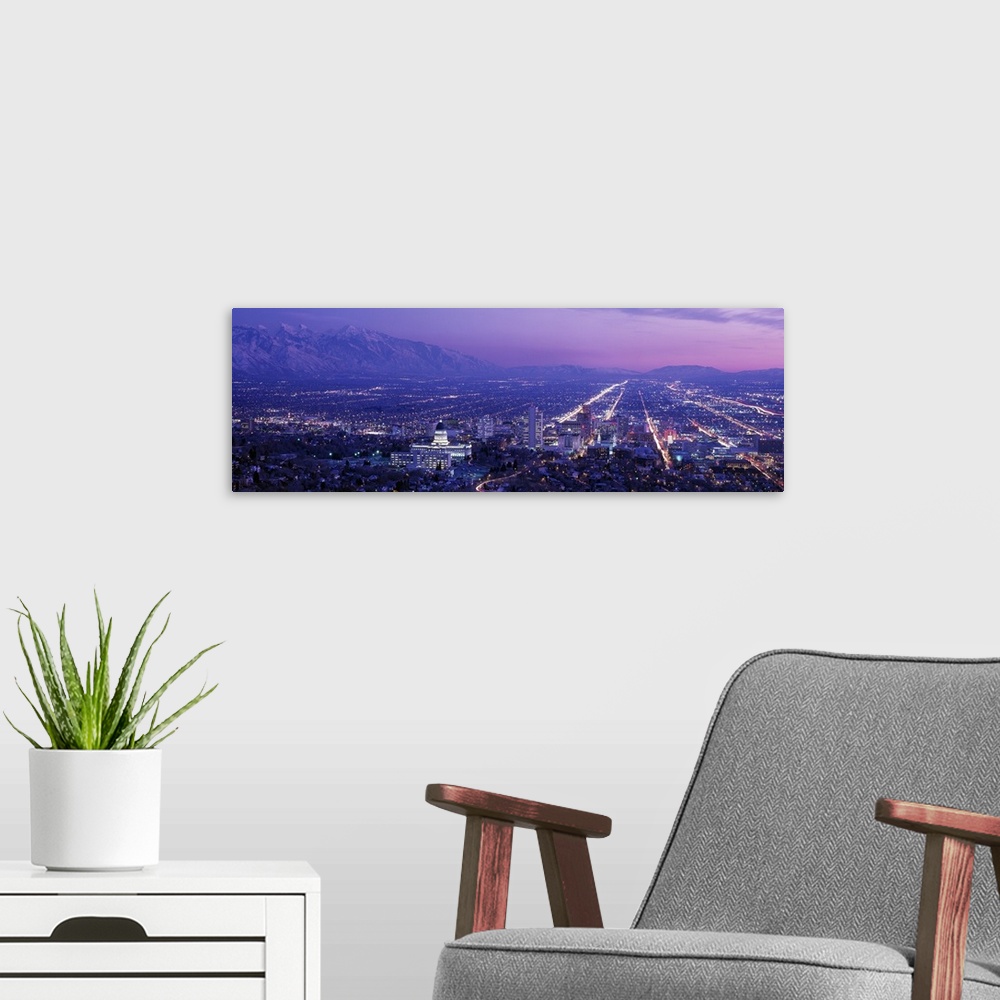 A modern room featuring High-angle panoramic photograph of city lit up at dusk with snow covered mountains in the distanc...
