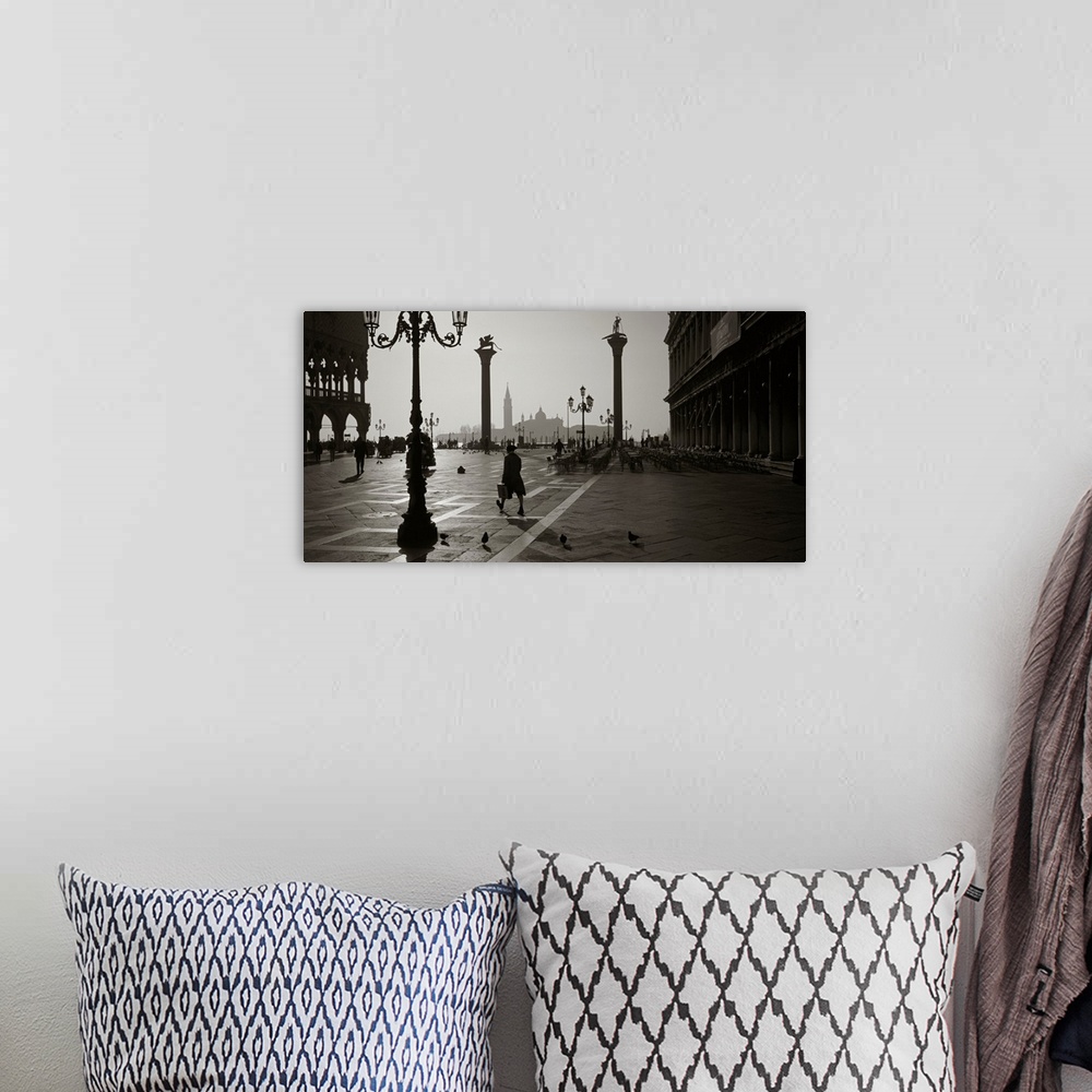 A bohemian room featuring Large monochromatic photograph displays a man walking across a brick covered square next to birds...