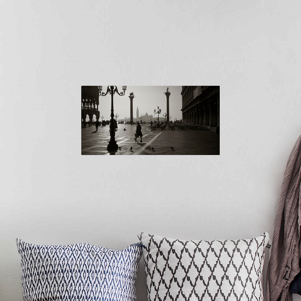 A bohemian room featuring Large monochromatic photograph displays a man walking across a brick covered square next to birds...