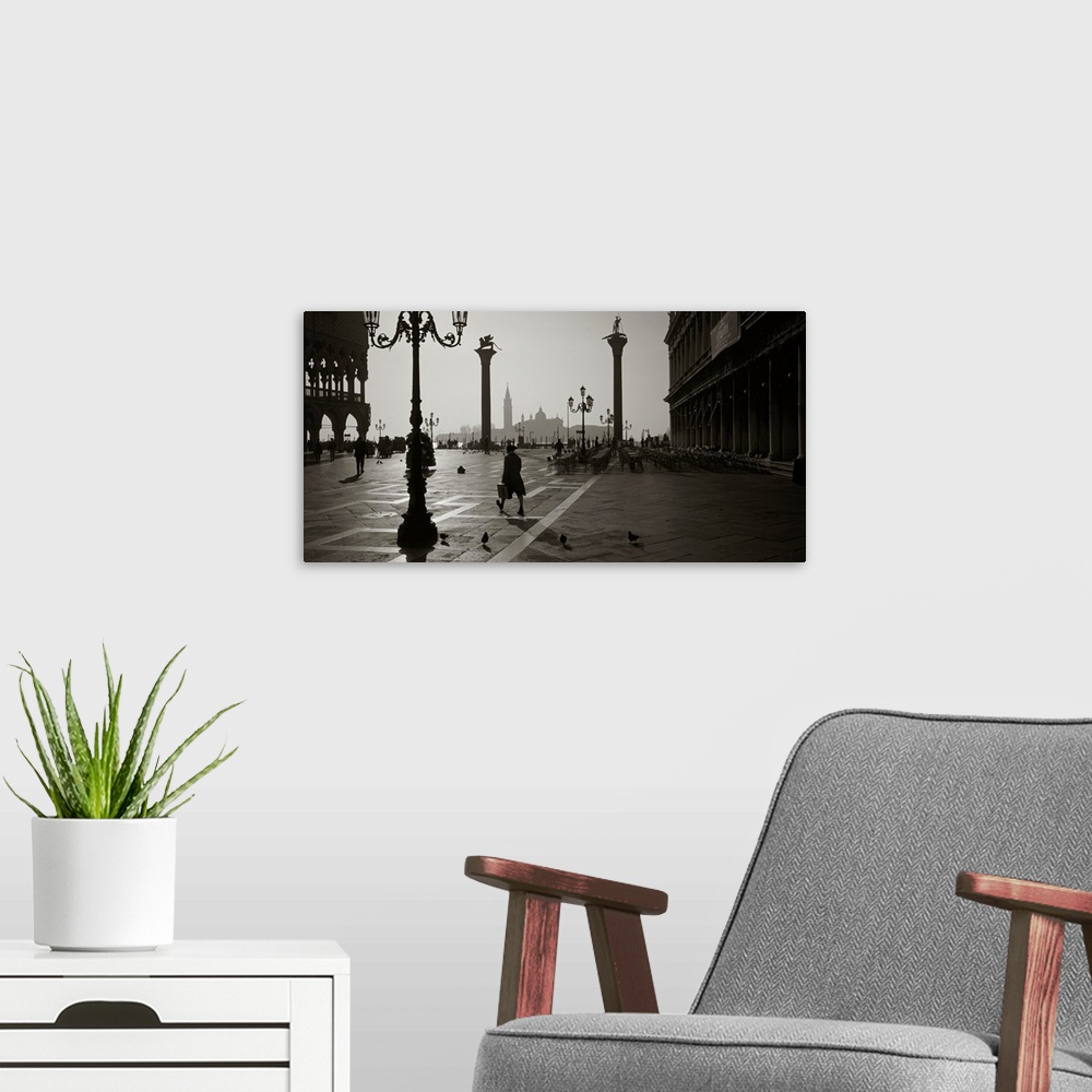 A modern room featuring Large monochromatic photograph displays a man walking across a brick covered square next to birds...