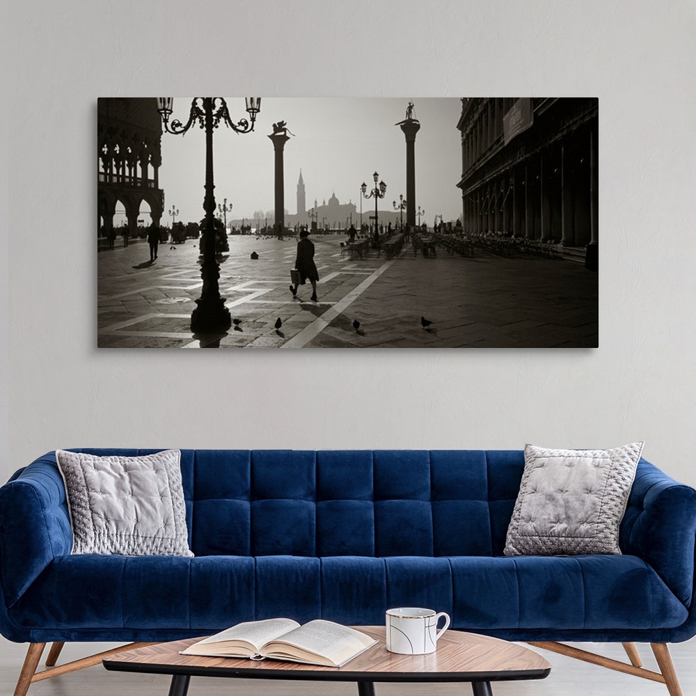 A modern room featuring Large monochromatic photograph displays a man walking across a brick covered square next to birds...