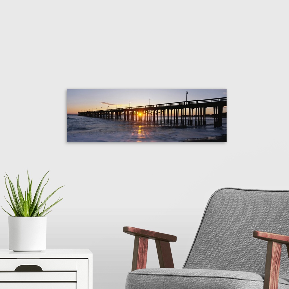 A modern room featuring Panoramic photo on canvas of the silhouette of a pier going out into the ocean against a sunset.