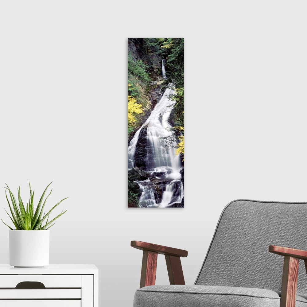 A modern room featuring Vertical, large photograph of Moss Glen Falls surrounded by rocky terrain and fall foliage, in th...