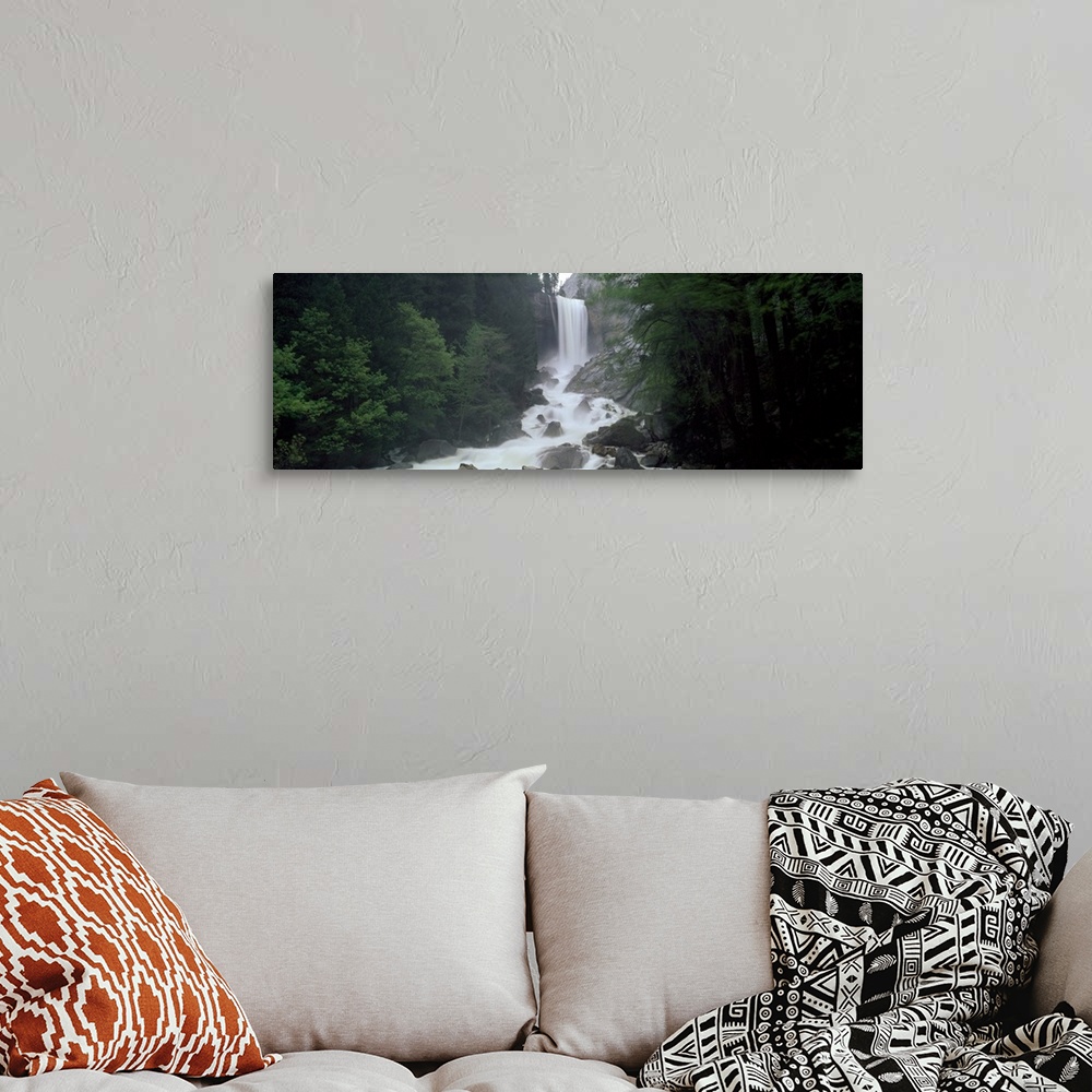 A bohemian room featuring Panoramic photograph of waterfall flowing into a rocky stream lined with thick dense forest.