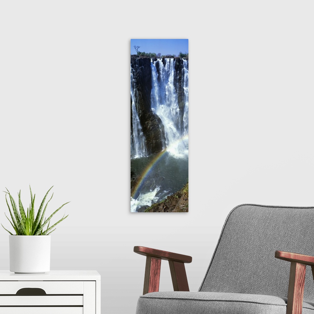 A modern room featuring A vertical panoramic piece of an immense waterfall with a rainbow stretching across the bottom of...