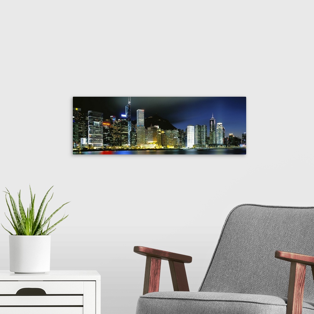 A modern room featuring Panoramic photograph of city skyline.  The buildings are lit up in the night sky and are reflecte...