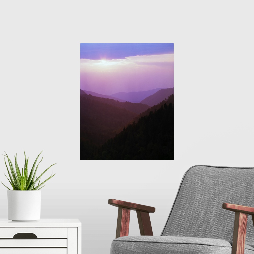 A modern room featuring Photograph of foggy mountain range under a cloudy sky with sun peeking through.