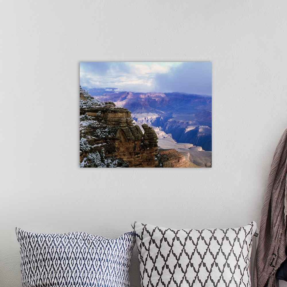 A bohemian room featuring Thick clouds hover over the Grand Canyon that is photographed from a distance behind a snowy cliff.