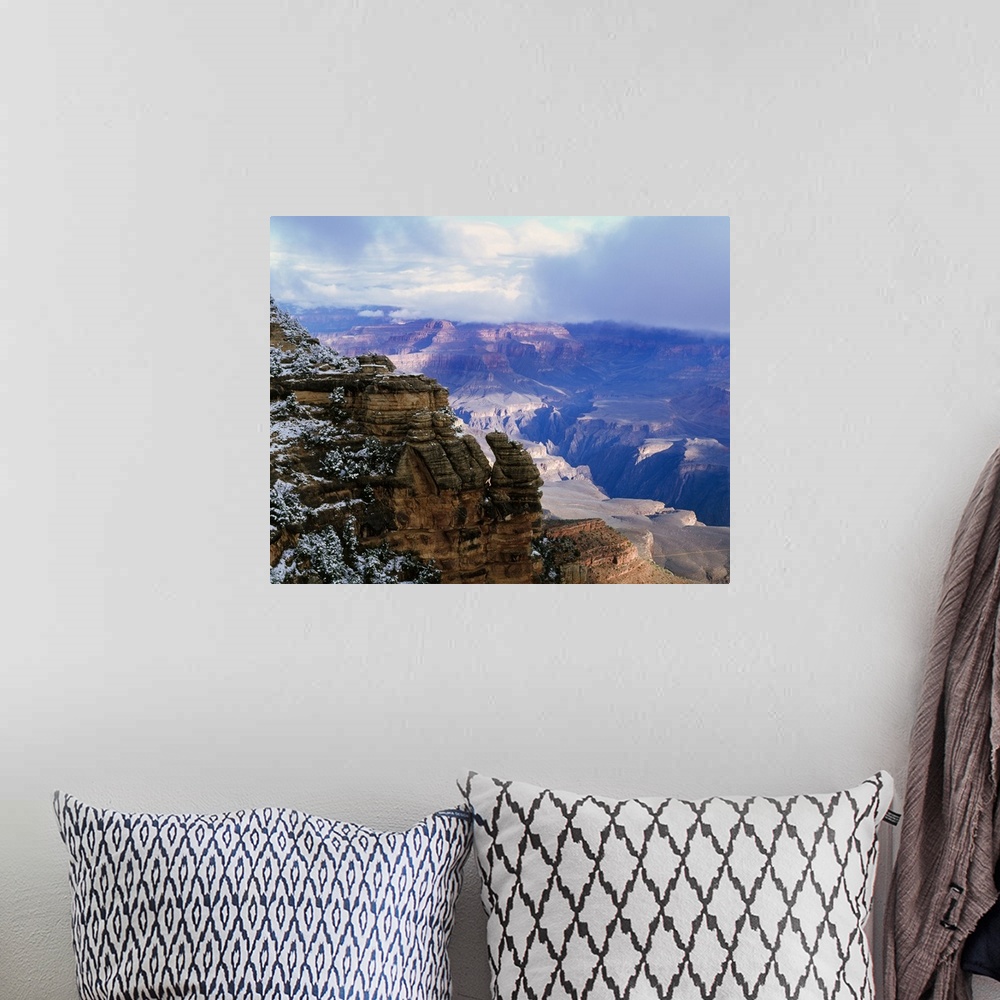 A bohemian room featuring Thick clouds hover over the Grand Canyon that is photographed from a distance behind a snowy cliff.