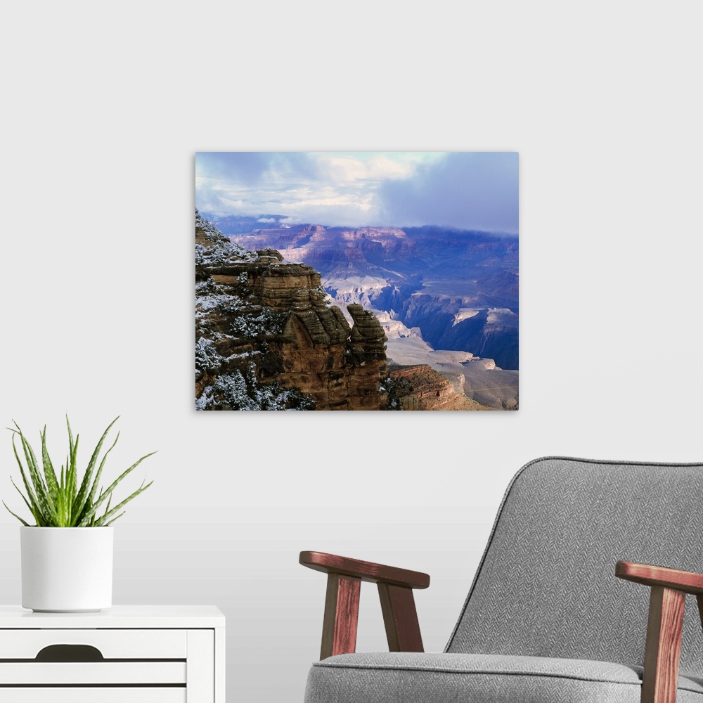 A modern room featuring Thick clouds hover over the Grand Canyon that is photographed from a distance behind a snowy cliff.