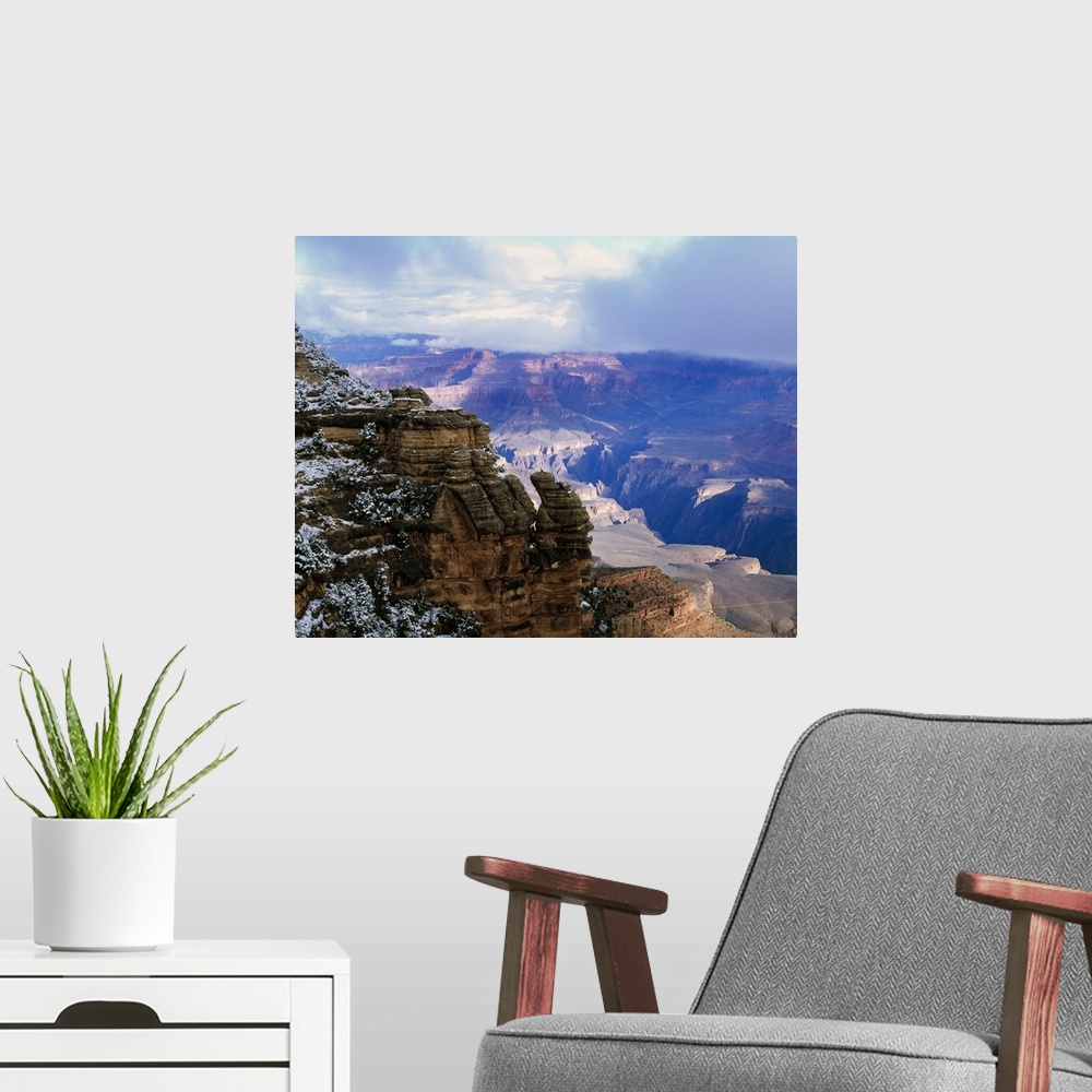 A modern room featuring Thick clouds hover over the Grand Canyon that is photographed from a distance behind a snowy cliff.