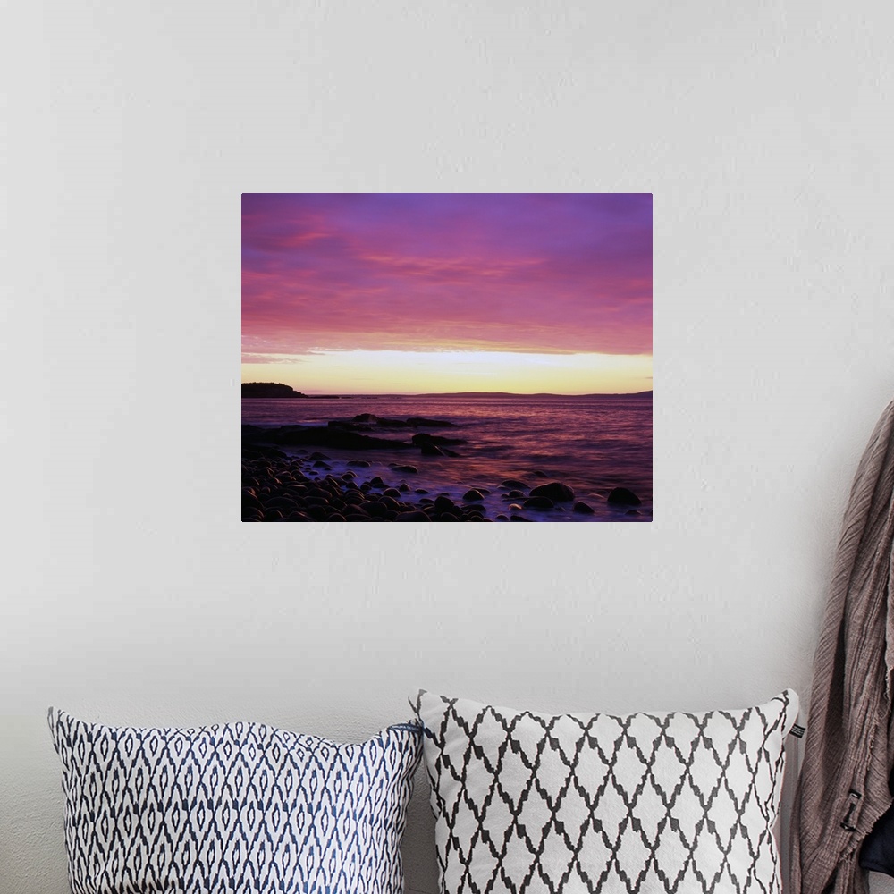 A bohemian room featuring This large piece is a picture taken of the sun rise off the coast of Maine. Rocks line the edge o...