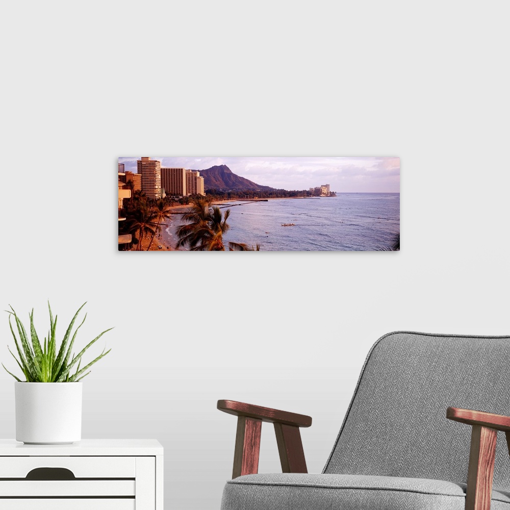 A modern room featuring A Hawaiian coast is photographed in wide angle view with a hotel sitting on the beach to the left...