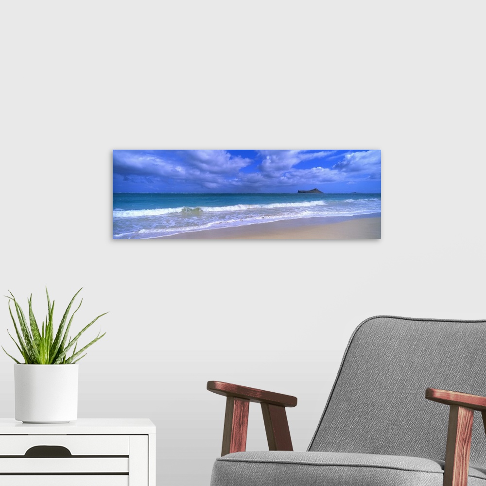 A modern room featuring Panoramic photograph of waves breaking on the beach during a cloudy day with island in the distan...