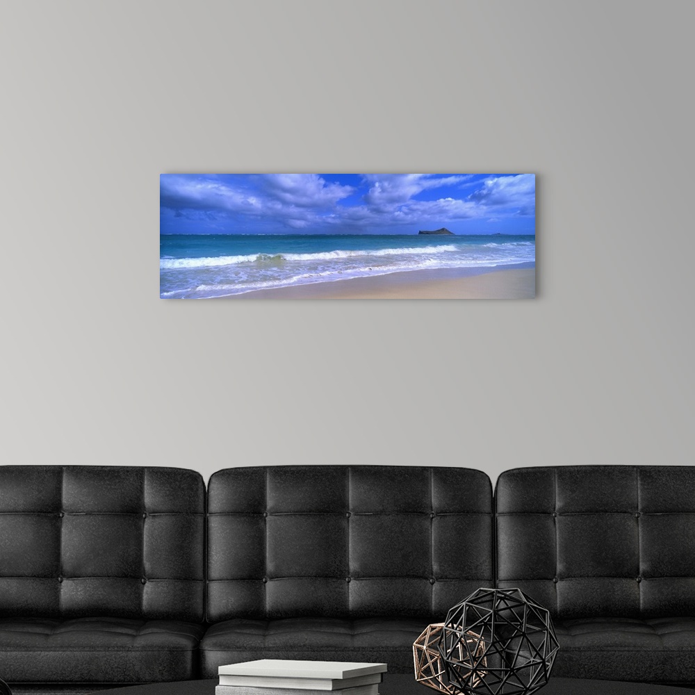A modern room featuring Panoramic photograph of waves breaking on the beach during a cloudy day with island in the distan...