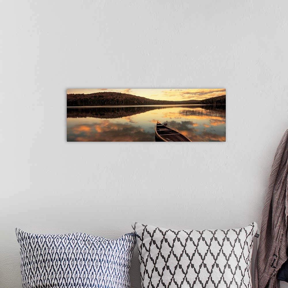 A bohemian room featuring A canoe floats in a still lake at sunset in New England as clouds reflect in the water.