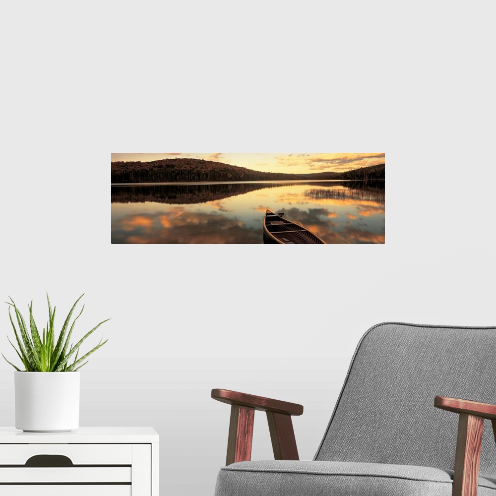 A modern room featuring A canoe floats in a still lake at sunset in New England as clouds reflect in the water.