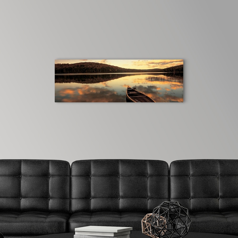 A modern room featuring A canoe floats in a still lake at sunset in New England as clouds reflect in the water.