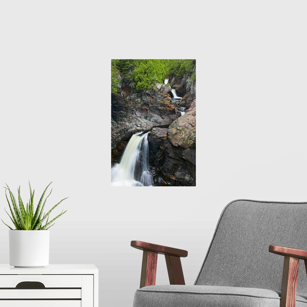 A modern room featuring This vertical nature photograph shows a rocky mountain face covered with trees and a river cuts t...