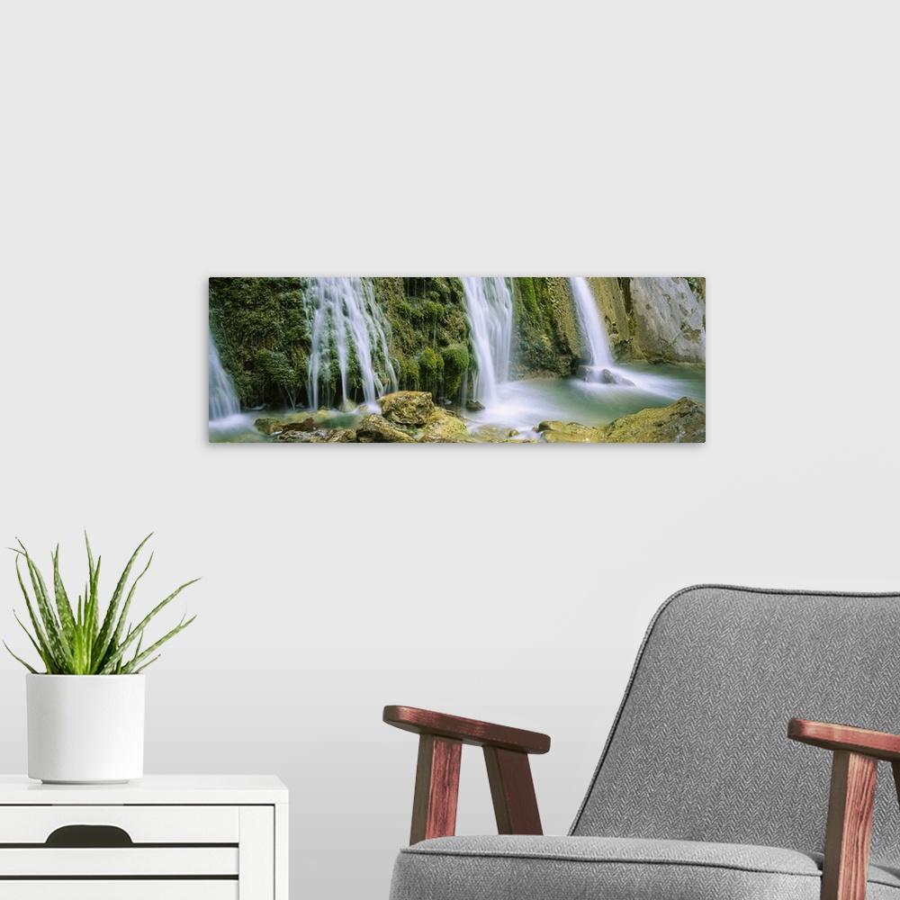 A modern room featuring Panoramic photograph taken of several waterfalls cascading over foliage and crashing onto rocks.
