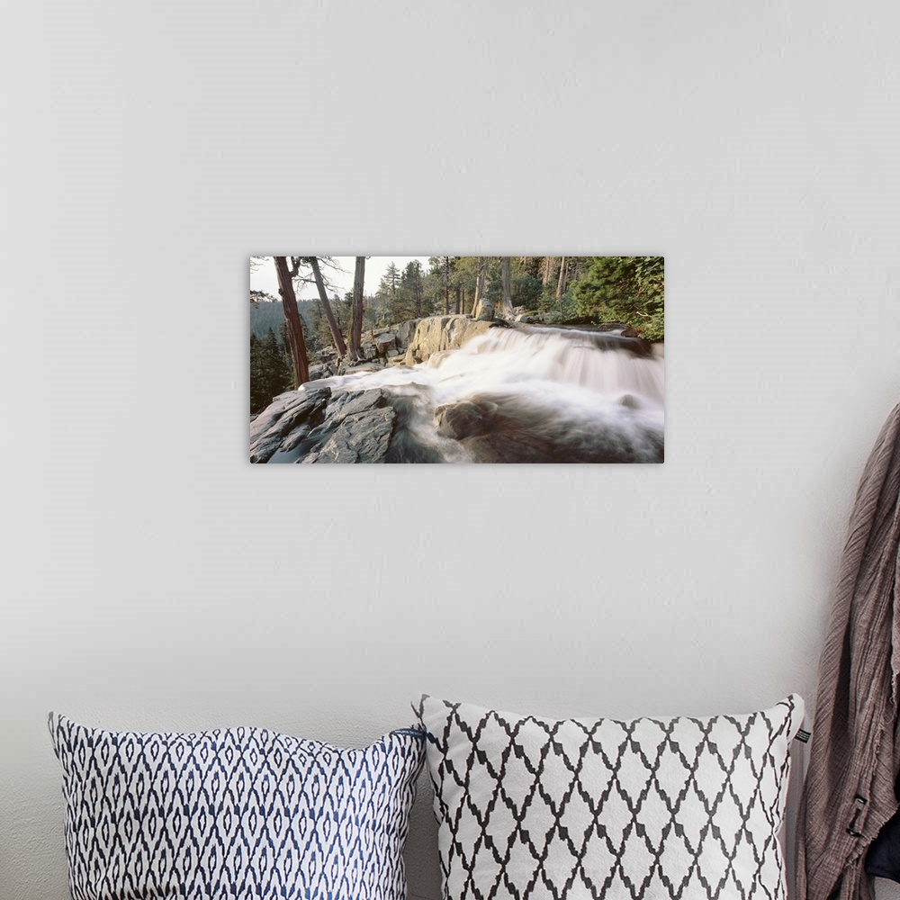 A bohemian room featuring A picture that has been taken of a waterfall flowing over large rocks and surrounded by a dense f...