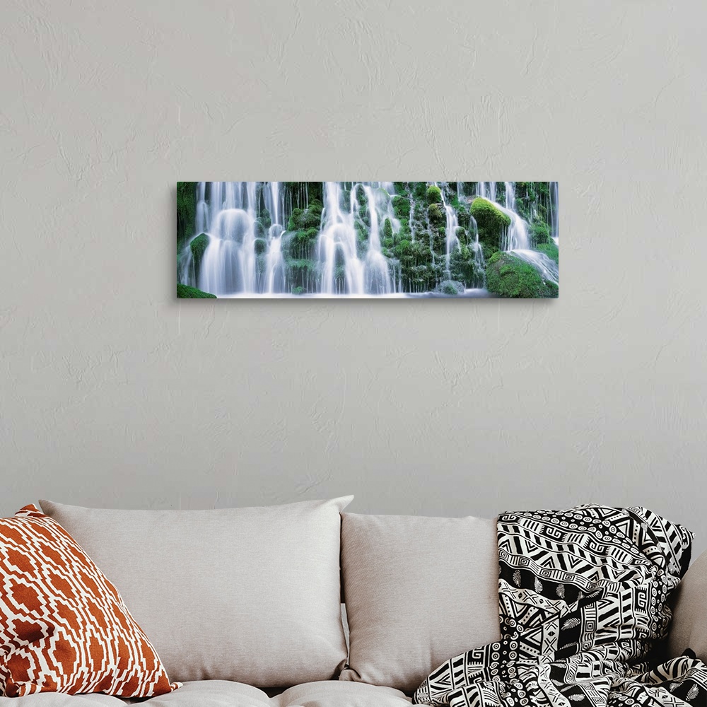 A bohemian room featuring A panoramic picture taken of a massive waterfall that flows over vast green foliage.