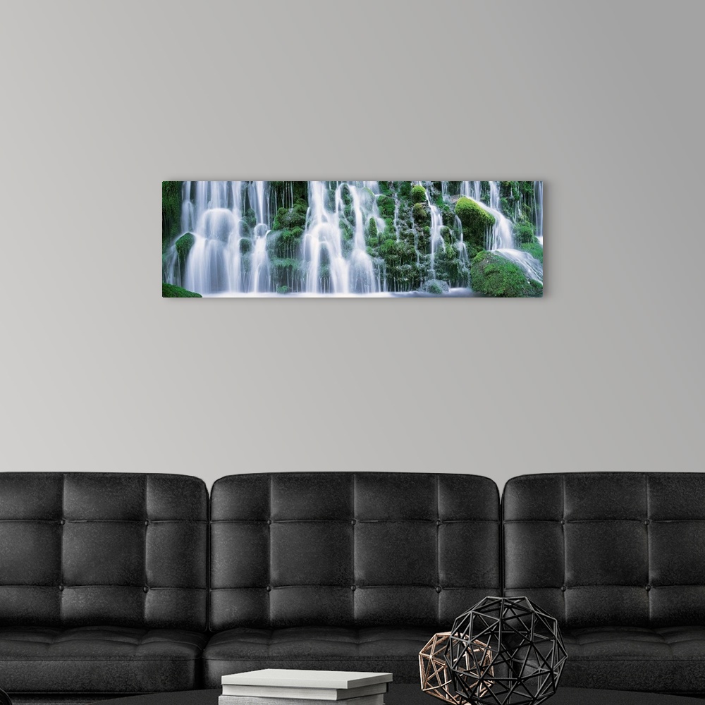 A modern room featuring A panoramic picture taken of a massive waterfall that flows over vast green foliage.