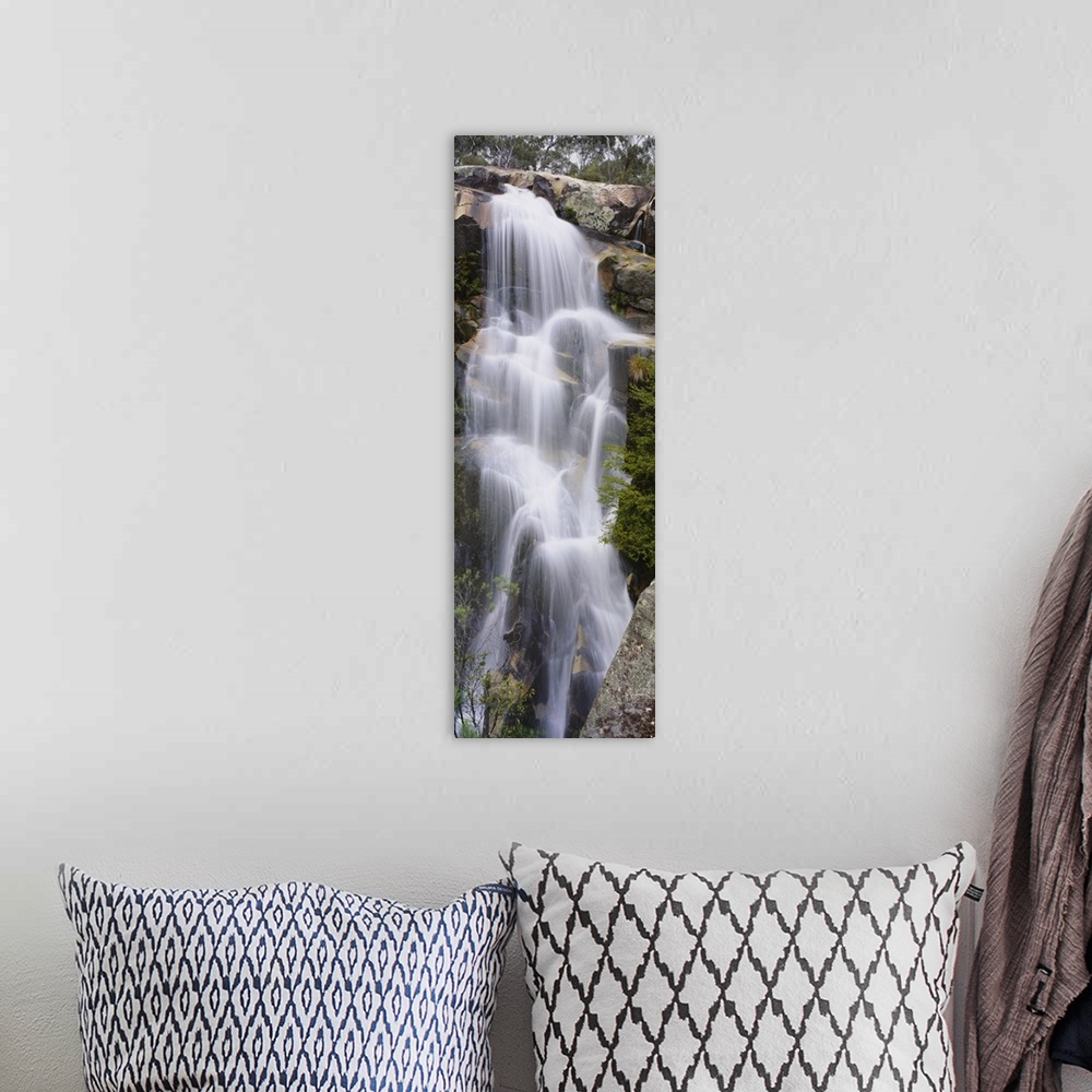 A bohemian room featuring This tall waterfall is pictured in an elongated view as it flows over large rocks.