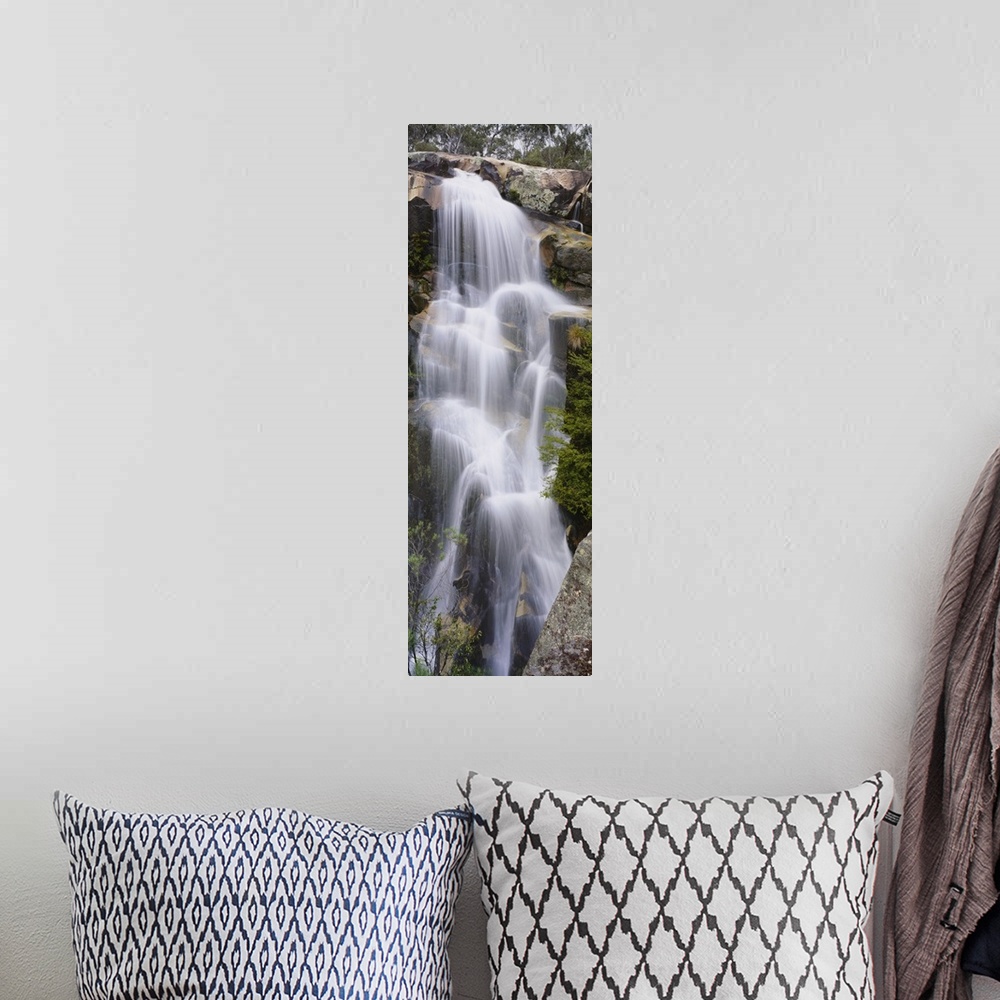 A bohemian room featuring This tall waterfall is pictured in an elongated view as it flows over large rocks.
