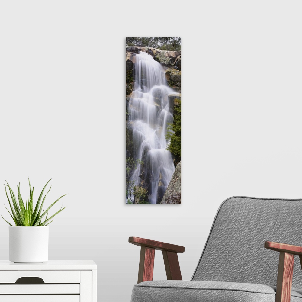 A modern room featuring This tall waterfall is pictured in an elongated view as it flows over large rocks.