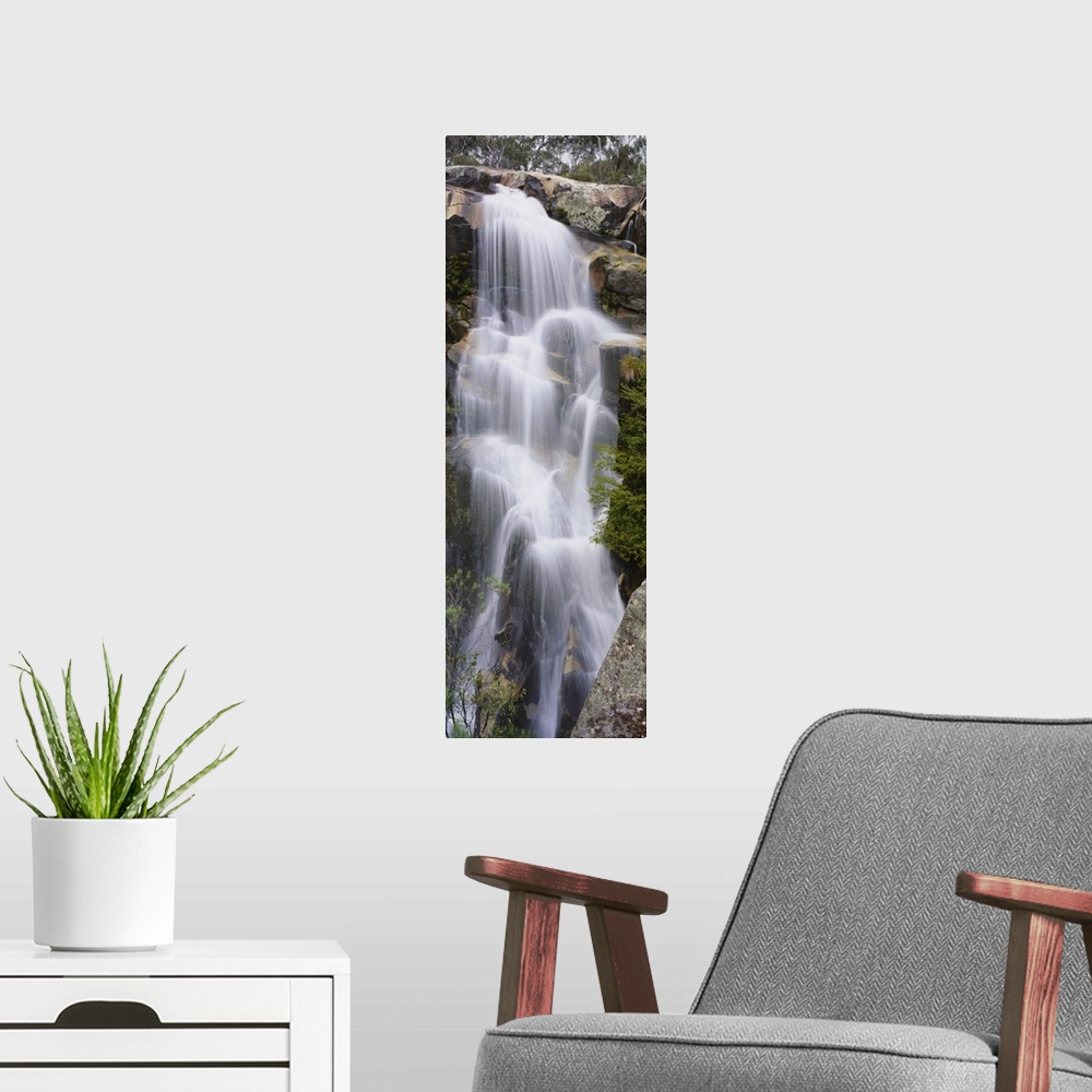 A modern room featuring This tall waterfall is pictured in an elongated view as it flows over large rocks.