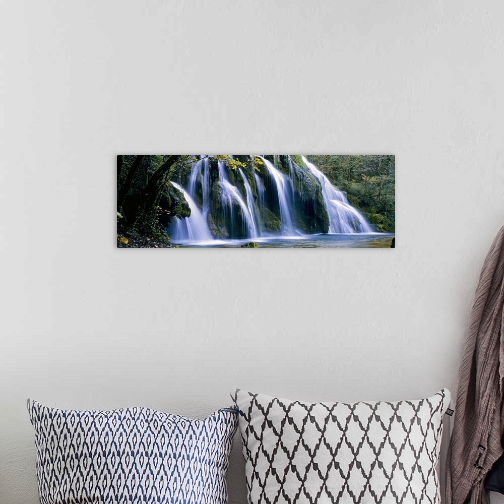 A bohemian room featuring Wide angle, large wall picture of a giant waterfall surrounded by a forest in Jura, France.