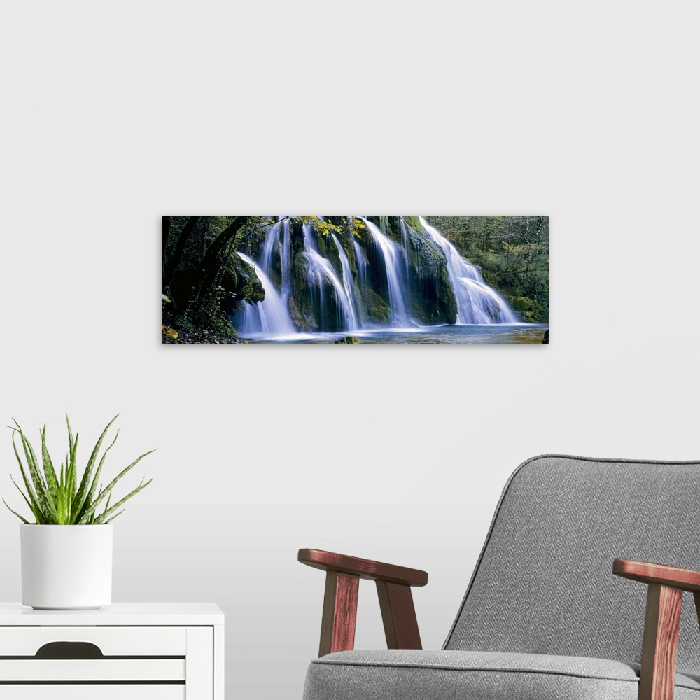 A modern room featuring Wide angle, large wall picture of a giant waterfall surrounded by a forest in Jura, France.