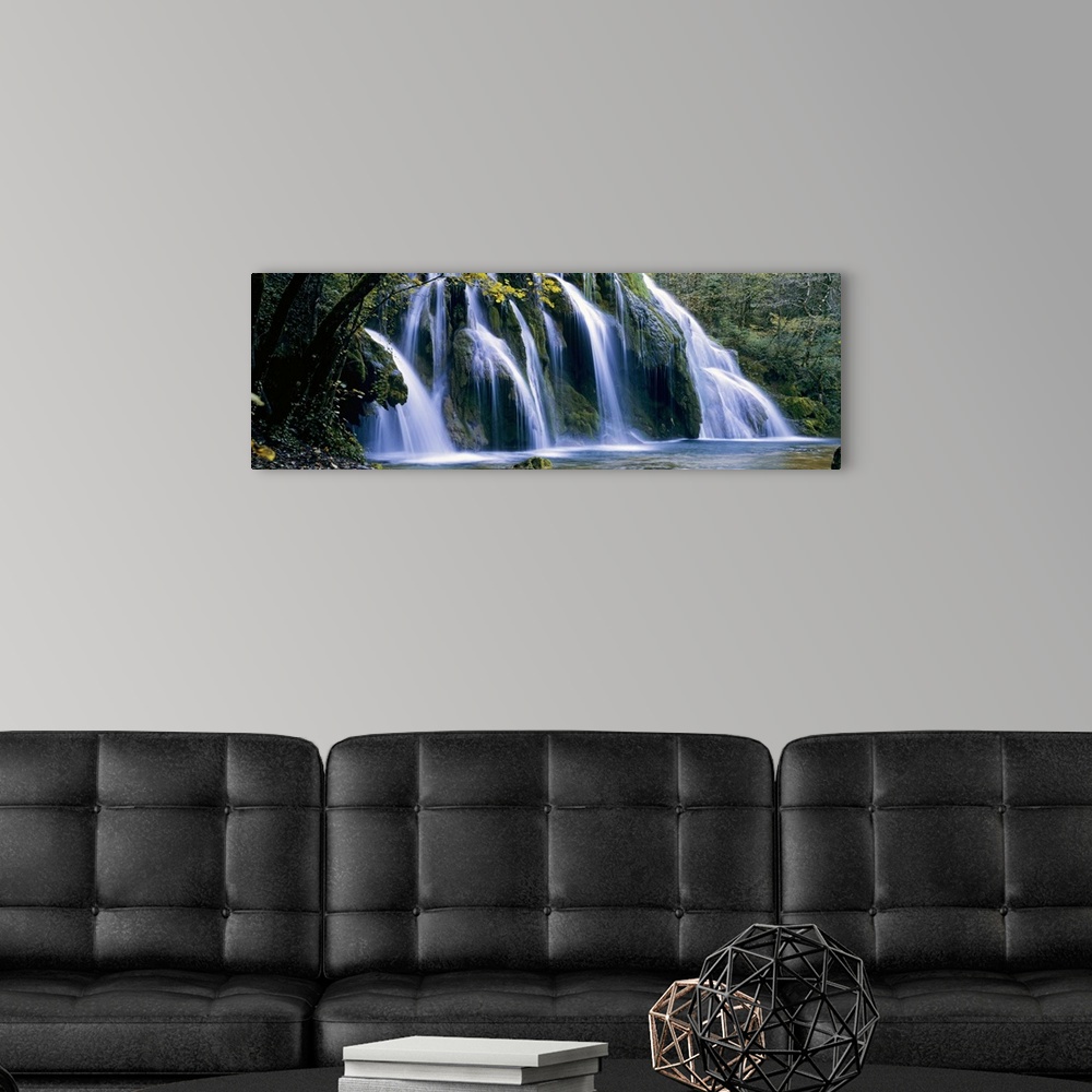 A modern room featuring Wide angle, large wall picture of a giant waterfall surrounded by a forest in Jura, France.
