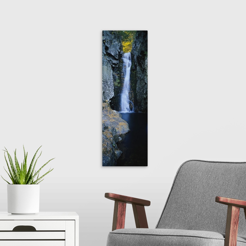 A modern room featuring Vertical photograph on a giant canvas of a large waterfall surrounded by the rocky edges of a for...