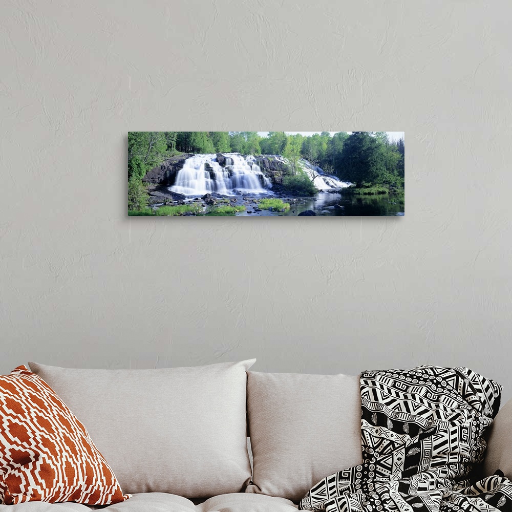 A bohemian room featuring Panoramic photograph on a giant wall hanging of a wide waterfall surrounded by a lush, green fore...