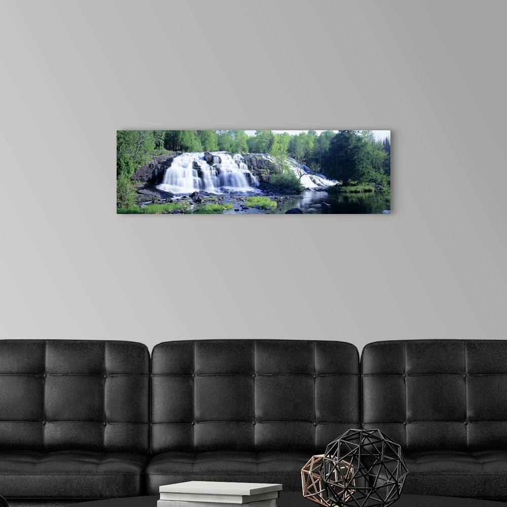 A modern room featuring Panoramic photograph on a giant wall hanging of a wide waterfall surrounded by a lush, green fore...