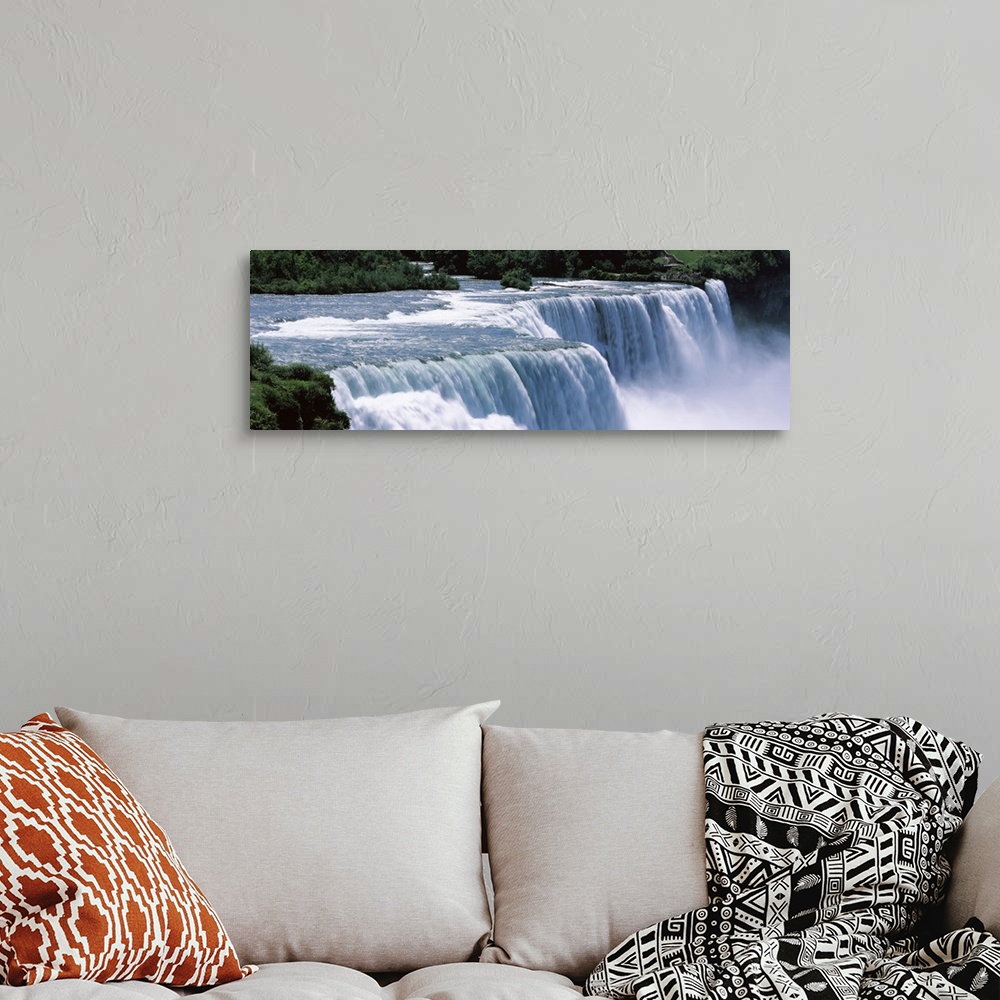 A bohemian room featuring A large panoramic photograph taken of Niagara falls with trees and foliage lining the back of the...